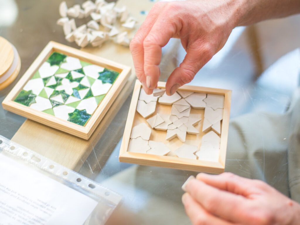 Handen leggen kleitegeltjes in een frame naast een afgewerkte groene onderzetter